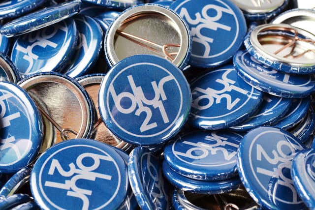 Stapel blauwe buttons van 25 mm met een wit logo