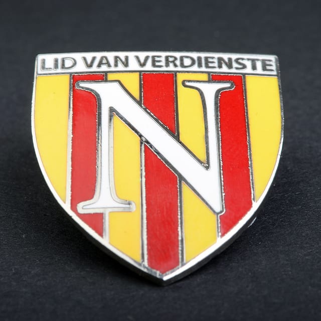 Hard emaille pin in schildvorm met een letter en rode en gele banen
