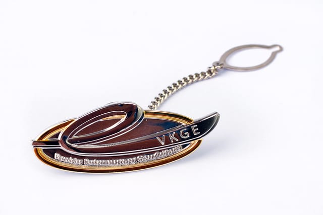 Goudkleurige logopin met emaille inkleuring en een kettinkje met klem